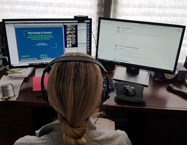 Nicole teaching an online class from her desk, headphones on, with two screens
