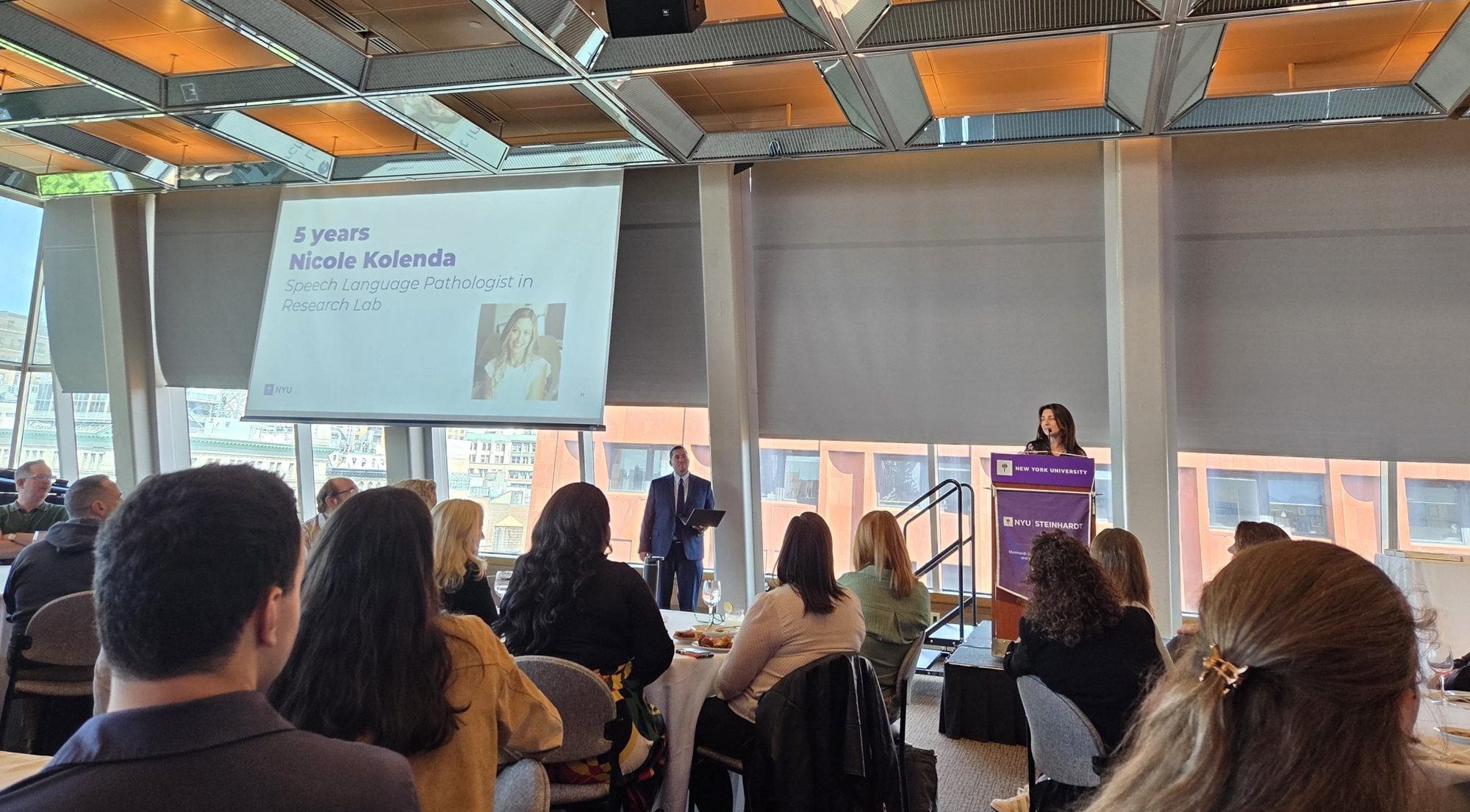 Nicole speaking at an NYU Steinhardt podium to a room of guests
