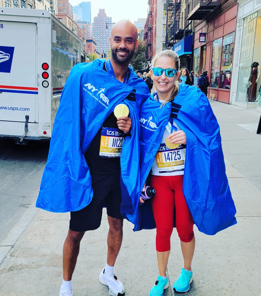 Nicole and a friend wrapped in finisher capes with their 2021 NYC Marathon medals