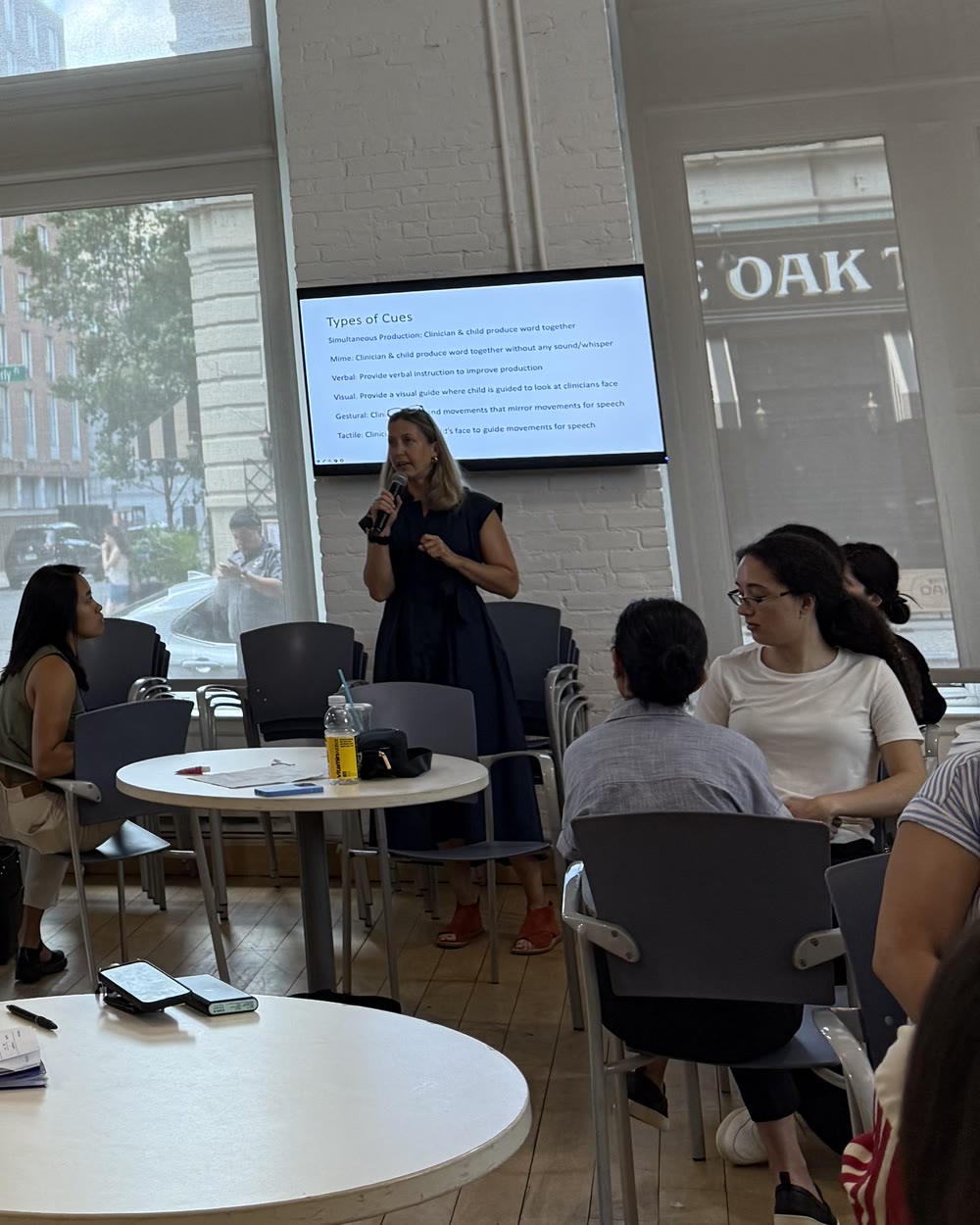 Nicole teaching a class of graduate students at NYU, with her slide on types of cues behind her