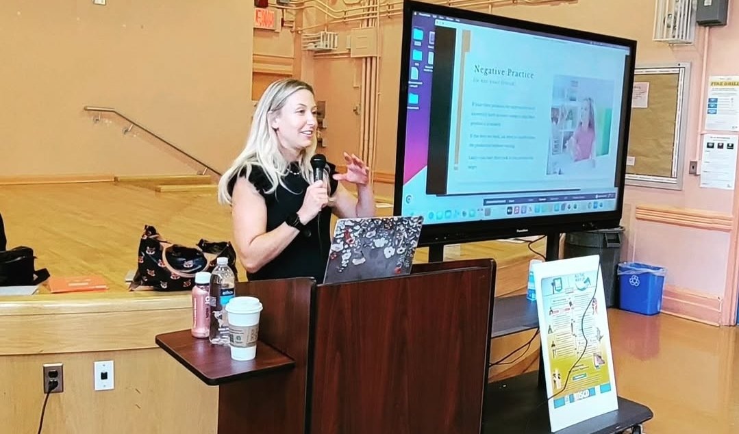 Nicole speaking at a podium beside her presentation slides